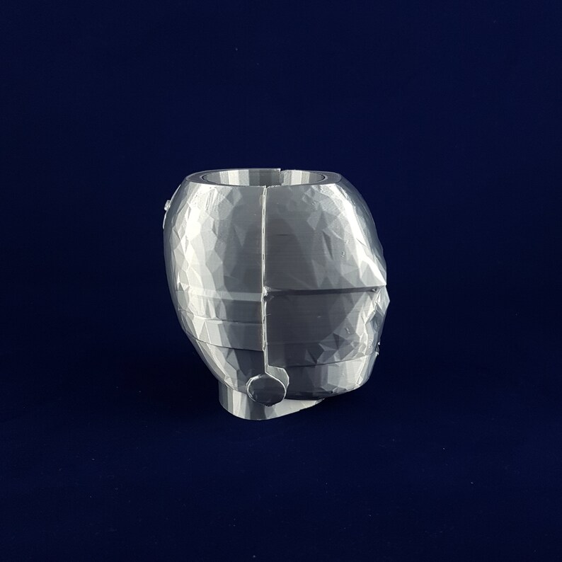 May include: A silver-coloured, geometrically-shaped planter with a textured surface. The planter is designed to resemble a head with a single ear.