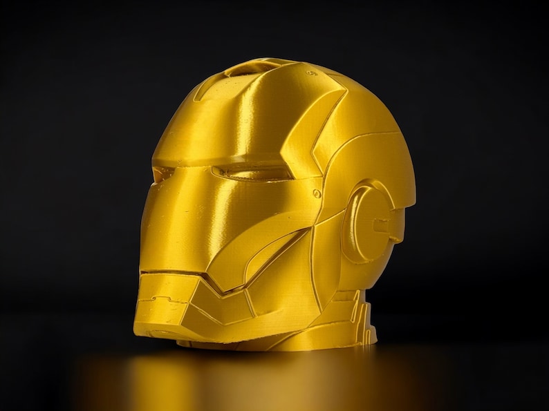 K&ouml;nnte beinhalten: Eine goldfarbene, im 3D-Druck hergestellte B&uuml;ste von Iron Mans Kopf. Die B&uuml;ste ist detailliert und hat eine metallische Oberfl&auml;che.