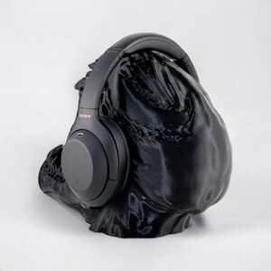 May include: Black over-ear headphones with the word "SONY" printed on the side, resting on a black fabric stand.