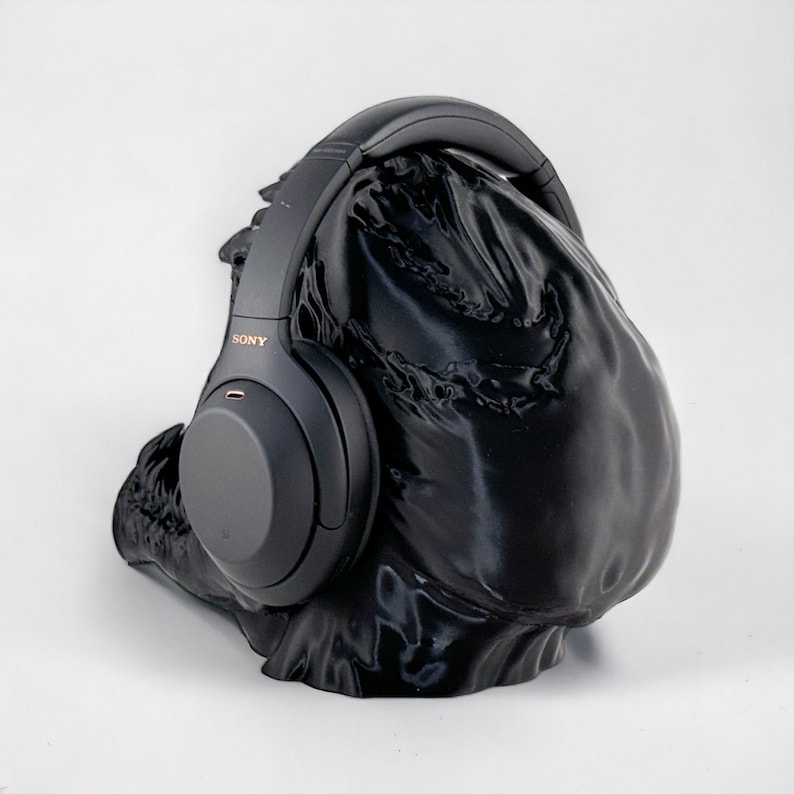 May include: Black over-ear headphones with the word "SONY" printed on the side, resting on a black fabric stand.