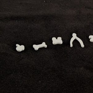 May include: A set of six white plastic cookie cutters in various shapes, including an apple, bone, house, pretzel, and two other shapes.