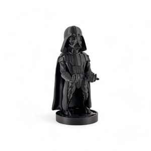 May include: A black Darth Vader figurine with a cape and a black base. The figurine is in a standing pose with its arms outstretched.