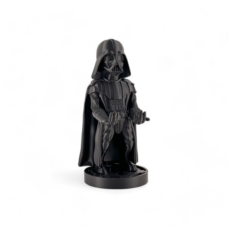 May include: A black Darth Vader figurine with a cape and a black base. The figurine is in a standing pose with its arms outstretched.