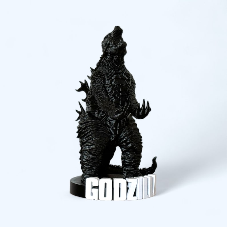 May include: Black Godzilla figurine with a textured surface, standing on a black base with the word "GODZILLA" printed in white.