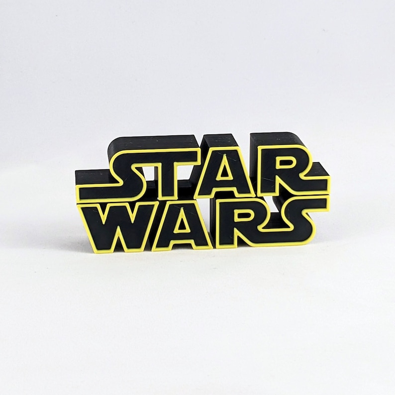 May include: Black 3D plastic sign with the text "STAR WARS" in yellow outlined letters.