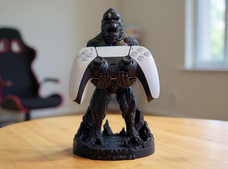 May include: A black and gray gorilla-shaped controller stand holding a white and black game controller. The stand is on a wooden table. The controller has a black center and white sides.