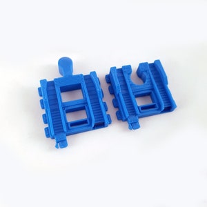 K&ouml;nnte beinhalten: Zwei blaue Plastik-Eisenbahnstreckenst&uuml;cke. Ein St&uuml;ck ist eine gerade Strecke mit zwei &Ouml;ffnungen. Das andere St&uuml;ck ist eine gebogene Strecke mit einer einzigen &Ouml;ffnung.
