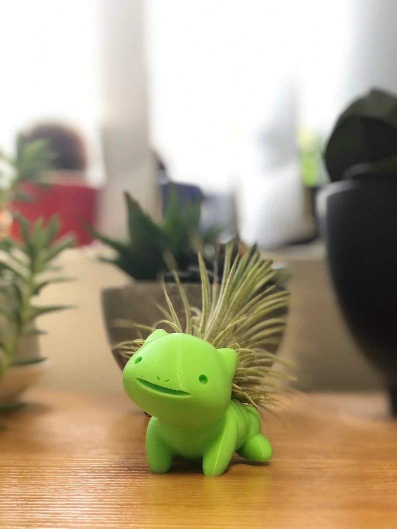 May include: A bright green, 3D printed planter shaped like a cartoon animal with a spiky, light green plant growing out of the top.