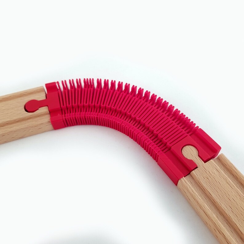 May include: A wooden train track with a red plastic flexible connector. The connector is made of multiple interlocking pieces that allow the track to bend.
