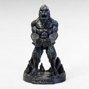 May include: A black gorilla statue with an open mouth and outstretched hands. The gorilla is standing on a rocky base. The statue is made of a dark material and has detailed textures.