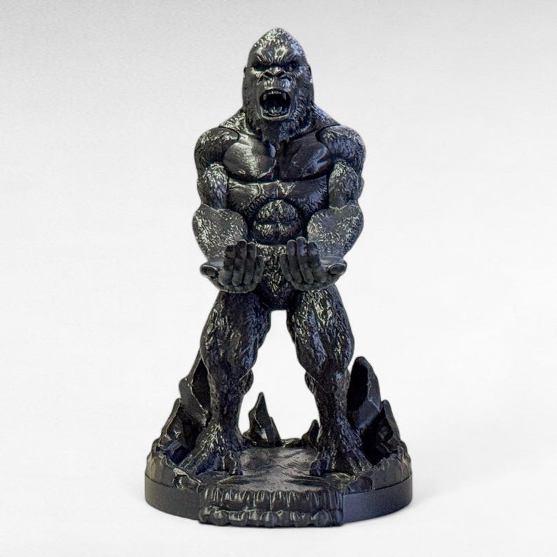 May include: A black gorilla statue with an open mouth and outstretched hands. The gorilla is standing on a rocky base. The statue is made of a dark material and has detailed textures.