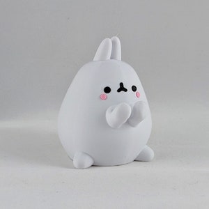 May include: White bunny figurine with pink cheeks and black eyes. The bunny is sitting with its paws raised in front of it.