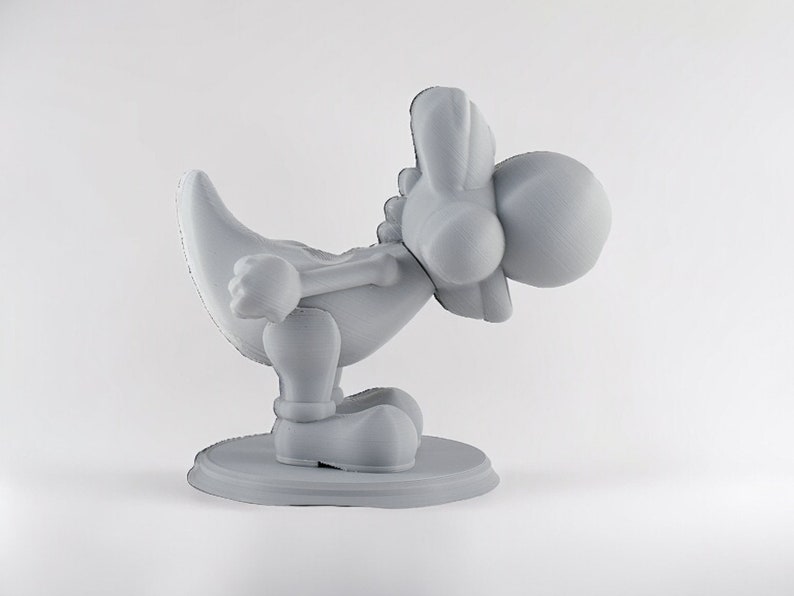 May include: A gray 3D printed figurine of a cartoon character with a long neck, large head, and a long tail. The character is in a crouching position with its head tilted down.