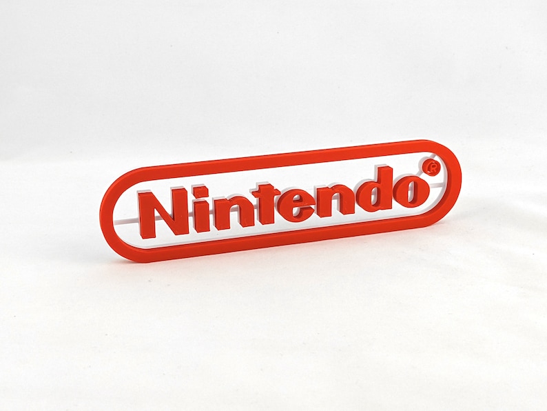 May include: A red plastic sign with the word "Nintendo" in white letters and a registered trademark symbol.