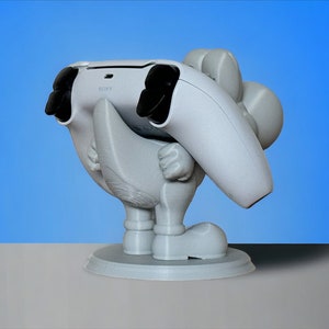 May include: White 3D printed figurine of a cartoon character holding a white PlayStation 5 controller. The character is standing on a round base.