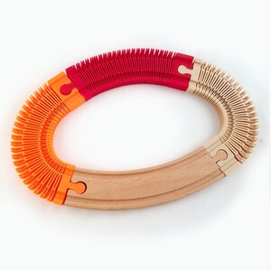 May include: A flexible wooden train track with orange, red, and beige flexible sections. The track is curved and forms a circle.