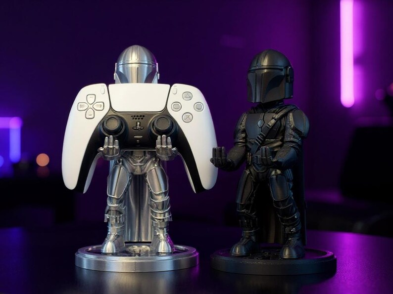 Pode incluir: Dois suportes para comando com o tema Mandalorian. Um &eacute; prateado e segura um comando PlayStation 5 branco e preto. O outro &eacute; preto e apresenta uma figura de Mandalorian. Ambos est&atilde;o em bases redondas.
