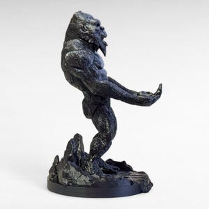 May include: A black gorilla statue in a dynamic pose, standing on a rocky base. The gorilla is sculpted with detailed fur and muscular definition, with its mouth open in a roar. The statue is a dark, matte finish.