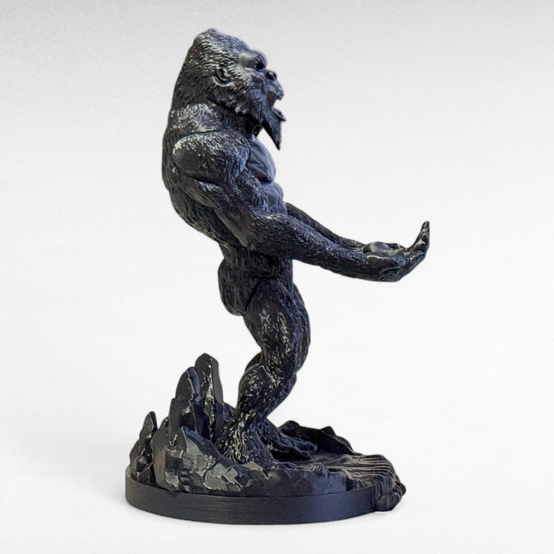 May include: A black gorilla statue in a dynamic pose, standing on a rocky base. The gorilla is sculpted with detailed fur and muscular definition, with its mouth open in a roar. The statue is a dark, matte finish.