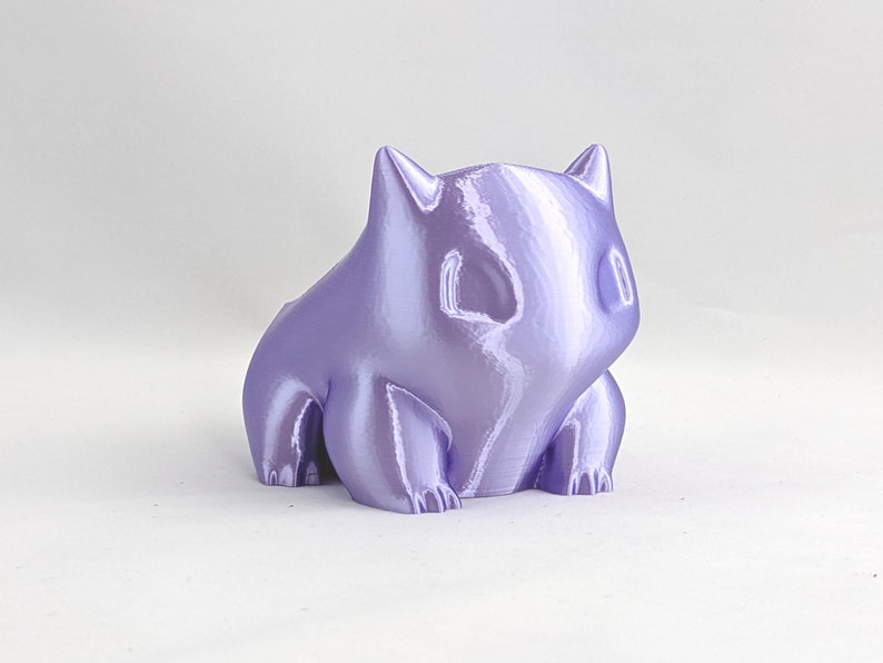 May include: A small, purple, 3D printed figurine of a cartoon character. The figurine has a rounded, slightly chubby body with a large head and small, pointed ears.