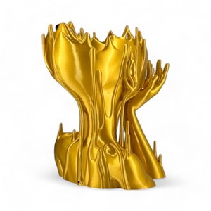 May include: A gold-coloured, abstract sculpture with a flowing, liquid-like design. The sculpture has a vase-like top and two arms reaching upwards.