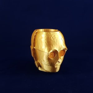 May include: A gold-coloured 3D printed planter shaped like the head of C-3PO from Star Wars. The planter has a textured surface and features the character's signature eyes and mouth.
