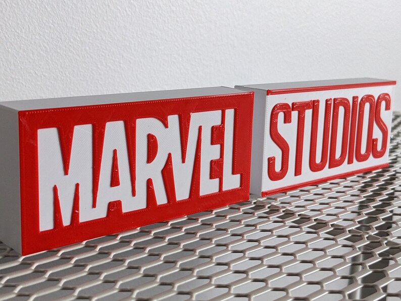 K&ouml;nnte beinhalten: Zwei rote Bl&ouml;cke mit wei&szlig;en Buchstaben. Der erste Block sagt "MARVEL" und der zweite Block sagt "STUDIOS".