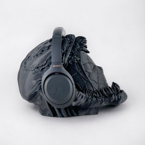 May include: Black wireless headphones with the word "SONY" printed on the side, resting on a black 3D printed stand shaped like a head.