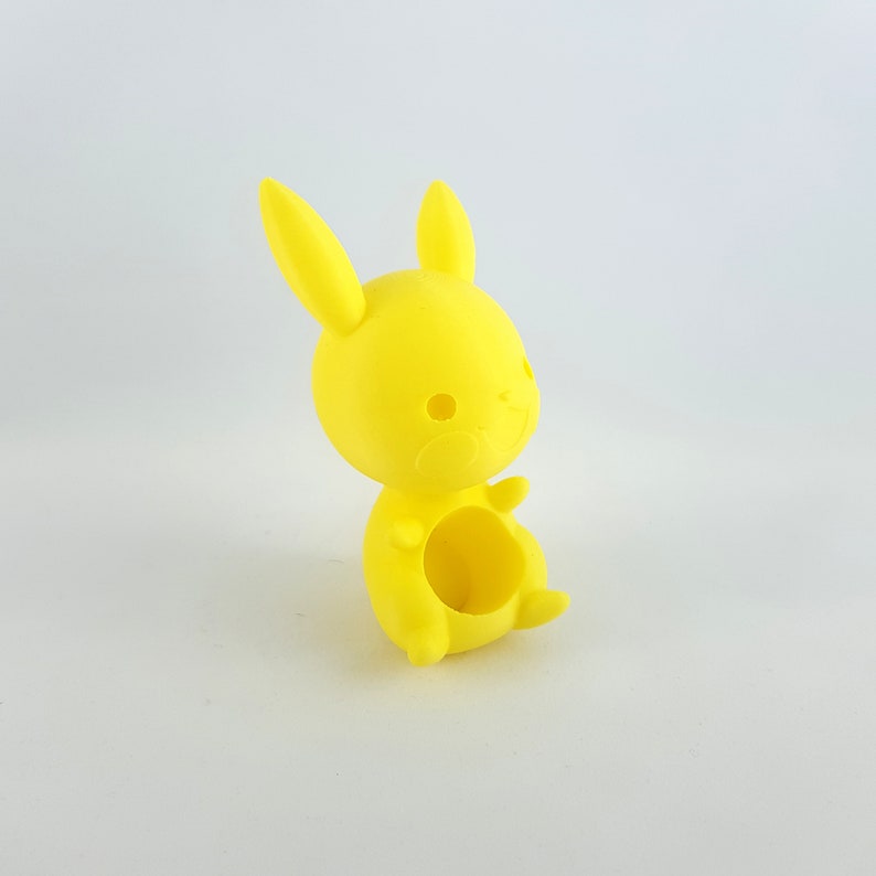 May include: A bright yellow 3D printed bunny figurine with a hollow center. The bunny has a simple, cartoon-like design with large ears and a small, round body.
