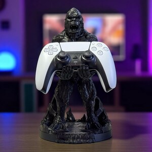 May include: A black gorilla statue holding a white and black video game controller. The statue has a detailed texture and is set on a round base. The controller has a sleek design with multiple buttons.
