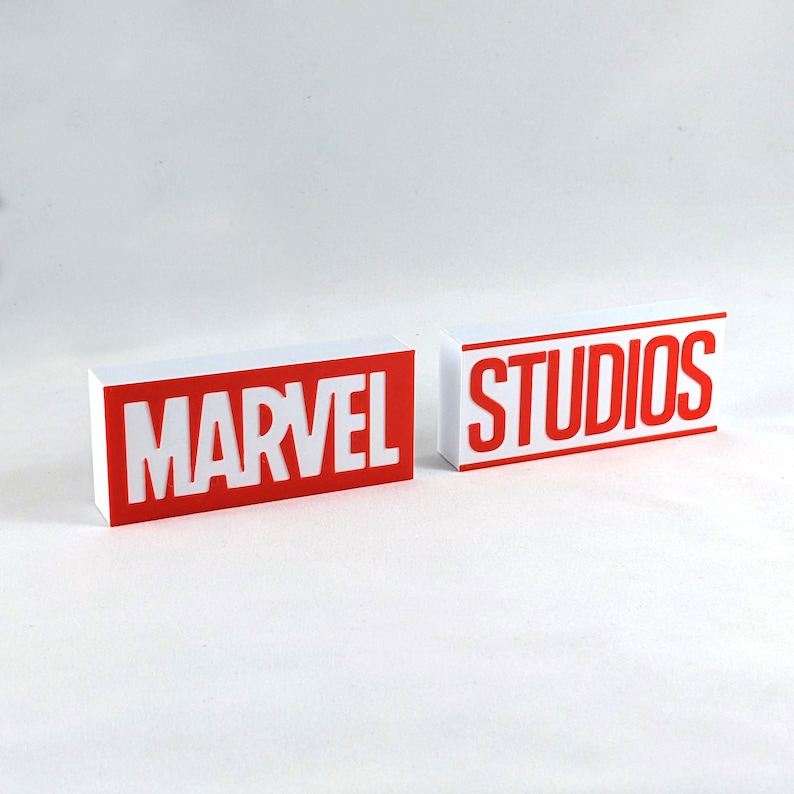 K&ouml;nnte beinhalten: Zwei wei&szlig;e Bl&ouml;cke mit roter Beschriftung. Der erste Block sagt "MARVEL" und der zweite Block sagt "STUDIOS".