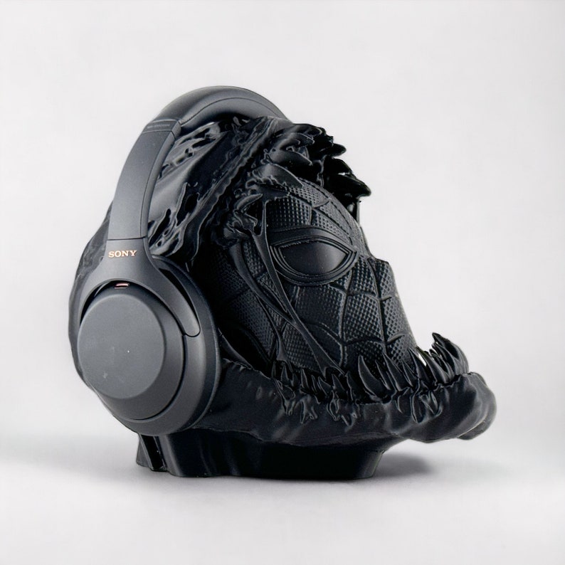 May include: Black headphones with a black and gray 3D printed stand shaped like a Venom character from Marvel Comics. The headphones have the word "SONY" printed on the side.