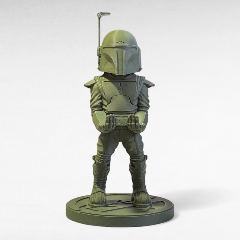 May include: A green figurine of a character in a helmet and armor, standing on a circular base. The figure has a detailed helmet with a vertical antenna and is holding its hands out in front. The figurine is approximately 6 inches tall.