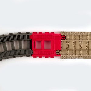 May include: A set of three toy train track pieces. The first piece is a curved gray track, the second is a red track with two square cutouts, and the third is a straight brown track with a textured surface.