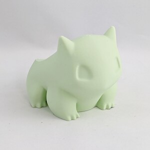 May include: A light green, 3D printed figurine of a Pokemon character. The figurine is sitting on a white surface.
