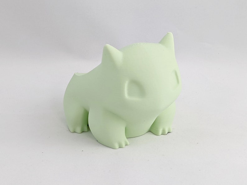 May include: A light green, 3D printed figurine of a Pokemon character. The figurine is sitting on a white surface.
