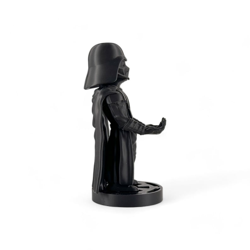 May include: A black Darth Vader figurine with a cape and a raised hand. The figurine is standing on a black base.
