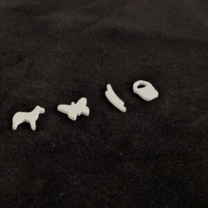 May include: Five white plastic figurines on a black background. The figurines are a horse, a butterfly, a curved line, a bucket, and a small circle.