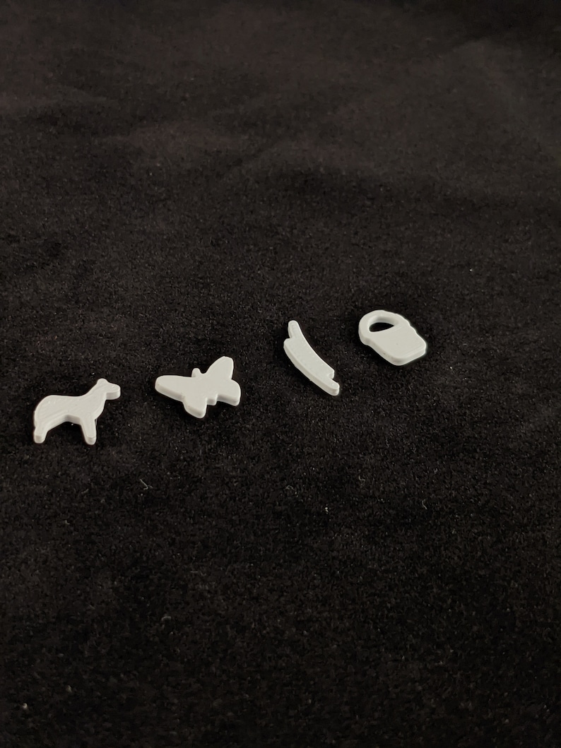May include: Five white plastic figurines on a black background. The figurines are a horse, a butterfly, a curved line, a bucket, and a small circle.