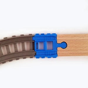 K&ouml;nnte beinhalten: Ein blauer Kunststoff-Verbindungsst&uuml;ck f&uuml;r eine Modelleisenbahn mit einem daran befestigten Holzschienenst&uuml;ck. Das Verbindungsst&uuml;ck hat ein kleines Fenster in der Mitte.