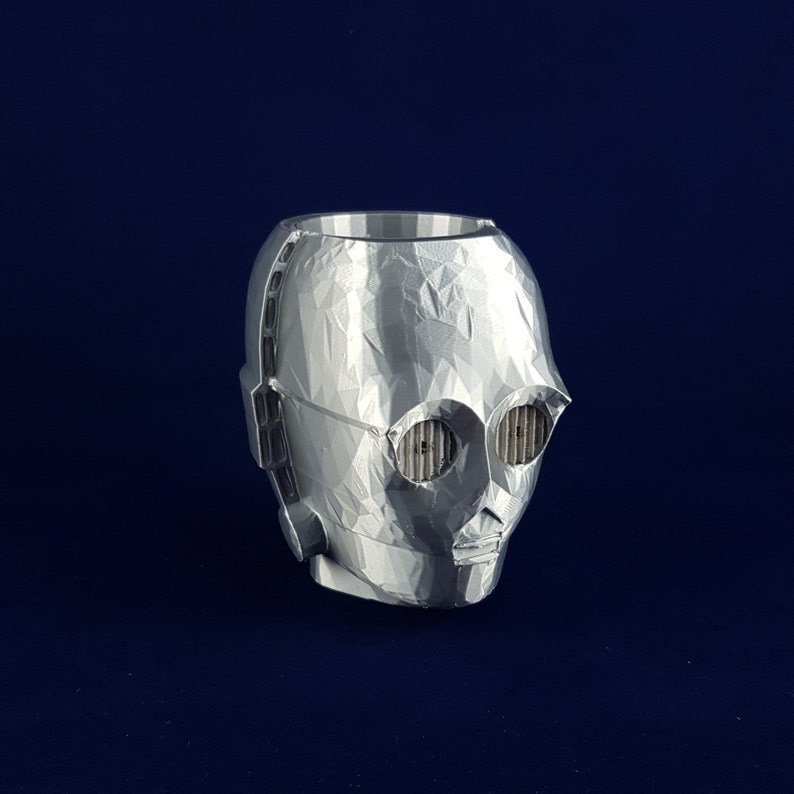 May include: A silver 3D printed planter shaped like the head of C-3PO from Star Wars. The planter has a textured surface and features the character's signature eyes and mouth.