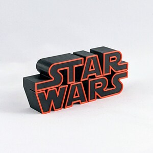 May include: Black plastic "Star Wars" logo with red outline. The logo is made of individual letters that are stacked on top of each other.