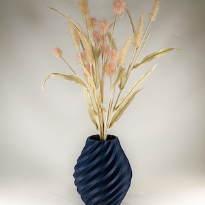 K&ouml;nnte beinhalten: Eine dunkelblaue, spiralf&ouml;rmige Vase mit einem Strau&szlig; getrockneter, hellbrauner Gr&auml;ser und rosa Bl&uuml;ten.
