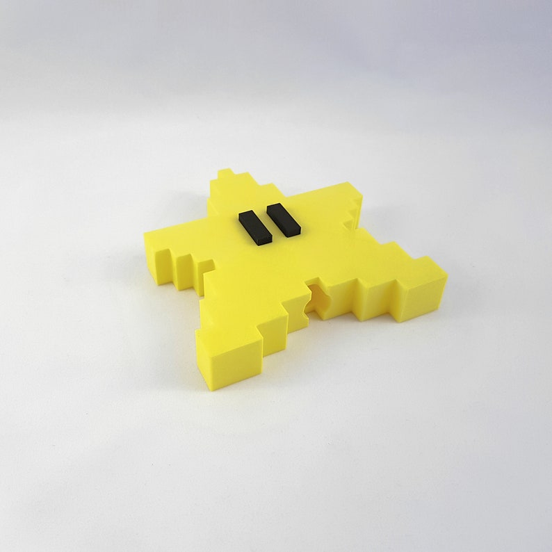 May include: A yellow star-shaped object with two black rectangles in the center. The object is made of a 3D printed material.