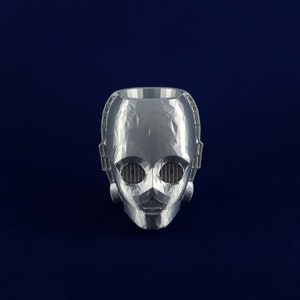 May include: A silver 3D printed robot head with a geometric design. The robot has two eyes and a mouth.