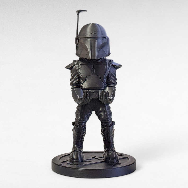 May include: A black figurine of a character from the Star Wars franchise, standing on a round base. The figure is wearing a helmet, armor, and boots. The figurine is a stylized representation of the character.