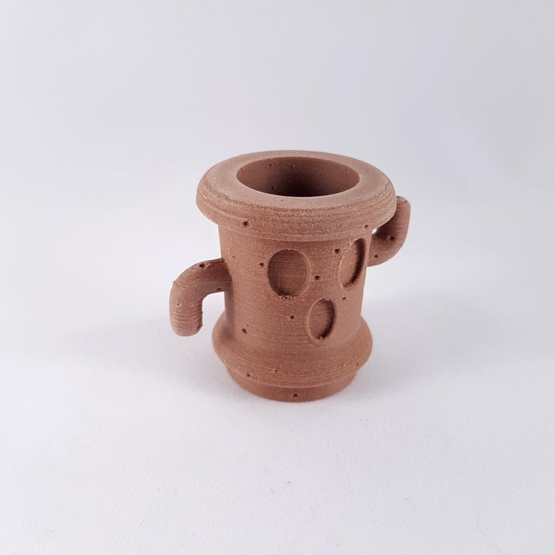 May include: A brown ceramic planter with two small arms, resembling a cactus. The planter has a textured surface and a circular opening at the top.