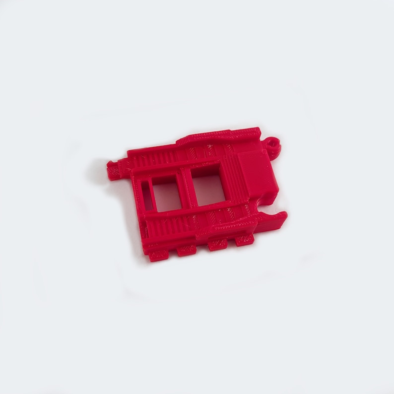 May include: A red plastic 3D printed part with two rectangular openings. The part has a textured surface and appears to be a component for a larger assembly.