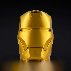 K&ouml;nnte beinhalten: Eine goldfarbene Metallskulptur eines Superheldenkopfes. Die Skulptur ist detailliert mit einer Maske und Gesichtsz&uuml;gen.