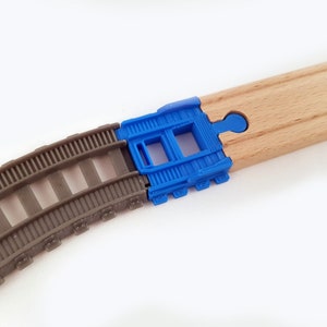 K&ouml;nnte beinhalten: Nahaufnahme einer Holz-Eisenbahnstrecke mit einem blauen Kunststoff-Verbindungsst&uuml;ck. Das Verbindungsst&uuml;ck hat zwei rechteckige &Ouml;ffnungen und ist so konzipiert, dass es zwei Streckenst&uuml;cke miteinander verbindet.
